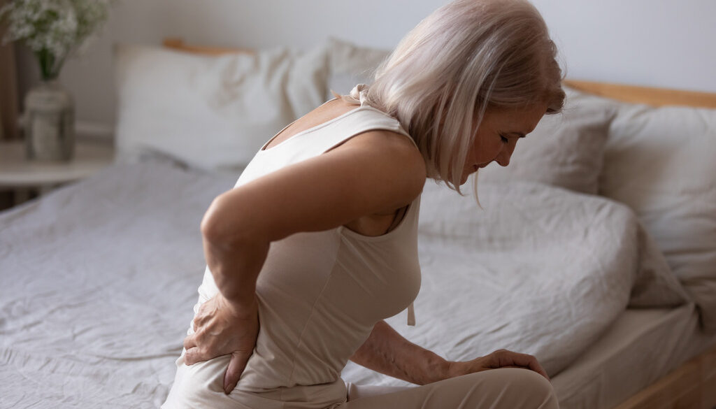 Woman Sitting on Her Bed Holding Her Lower Back How to Prevent Osteoporosis After Menopause