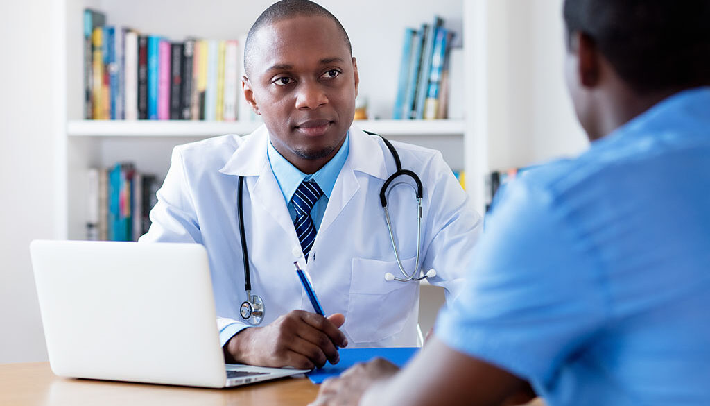 An African American Doctor Sitting at a Desk Listening Intently to a Patient Who Should See an Internist